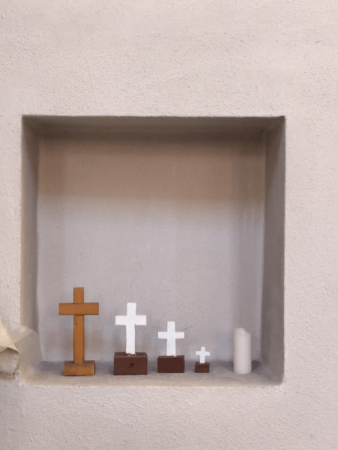 Vier Kreuze und eine Kerze in einer Nische.