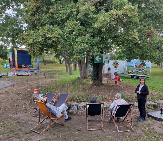 Station "die Bäume stehen voller Laub"; Besucher des Gottesdienstes liegen auf Liegestühlen und schauen in eine Baumkrone.