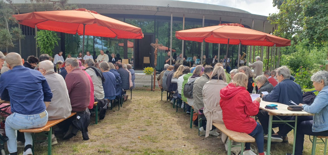 Die Besucher des ökumenischen Himmelfahrtsgottesdienstes sitzen an Biertischgarnituren im Garten der Umweltstation in Würzburg