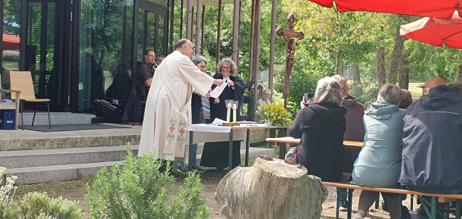 Der katholische Diakon und die evangelische Pfarrerin halten das Blatt fest, damit die Lektorin den Predigttext lesen kann.